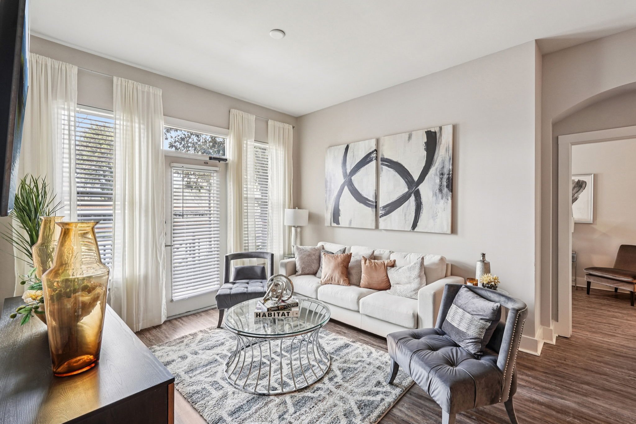 A living room with a grey sofa, a glass coffee table, and a large abstract painting on the wall.